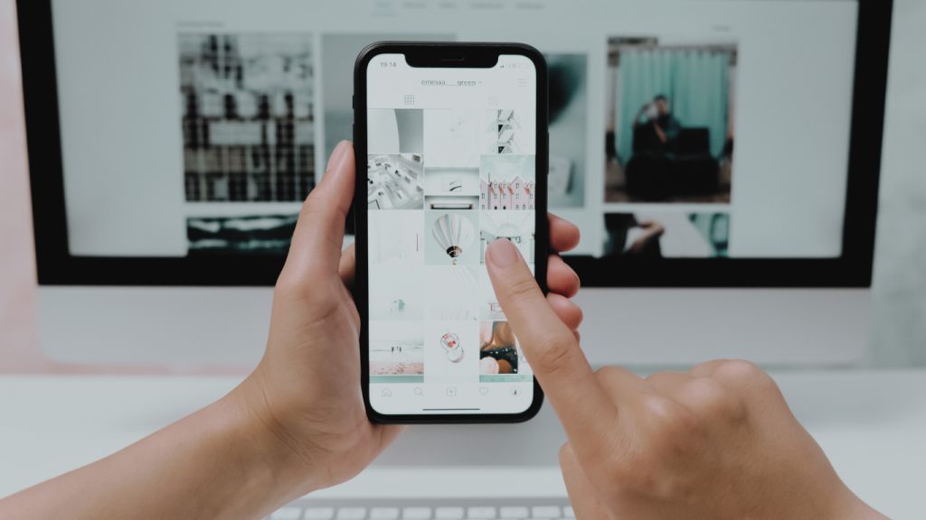 Phone showing a social media feed in front of a monitor